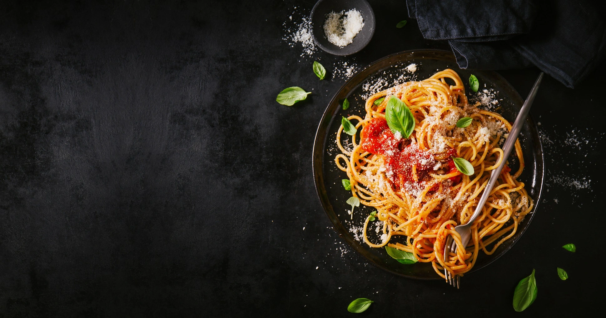 A plate of spaghetti topped with red tomato sauce, Parmesan cheese, fresh ground pepper,and fresh basil leaves.